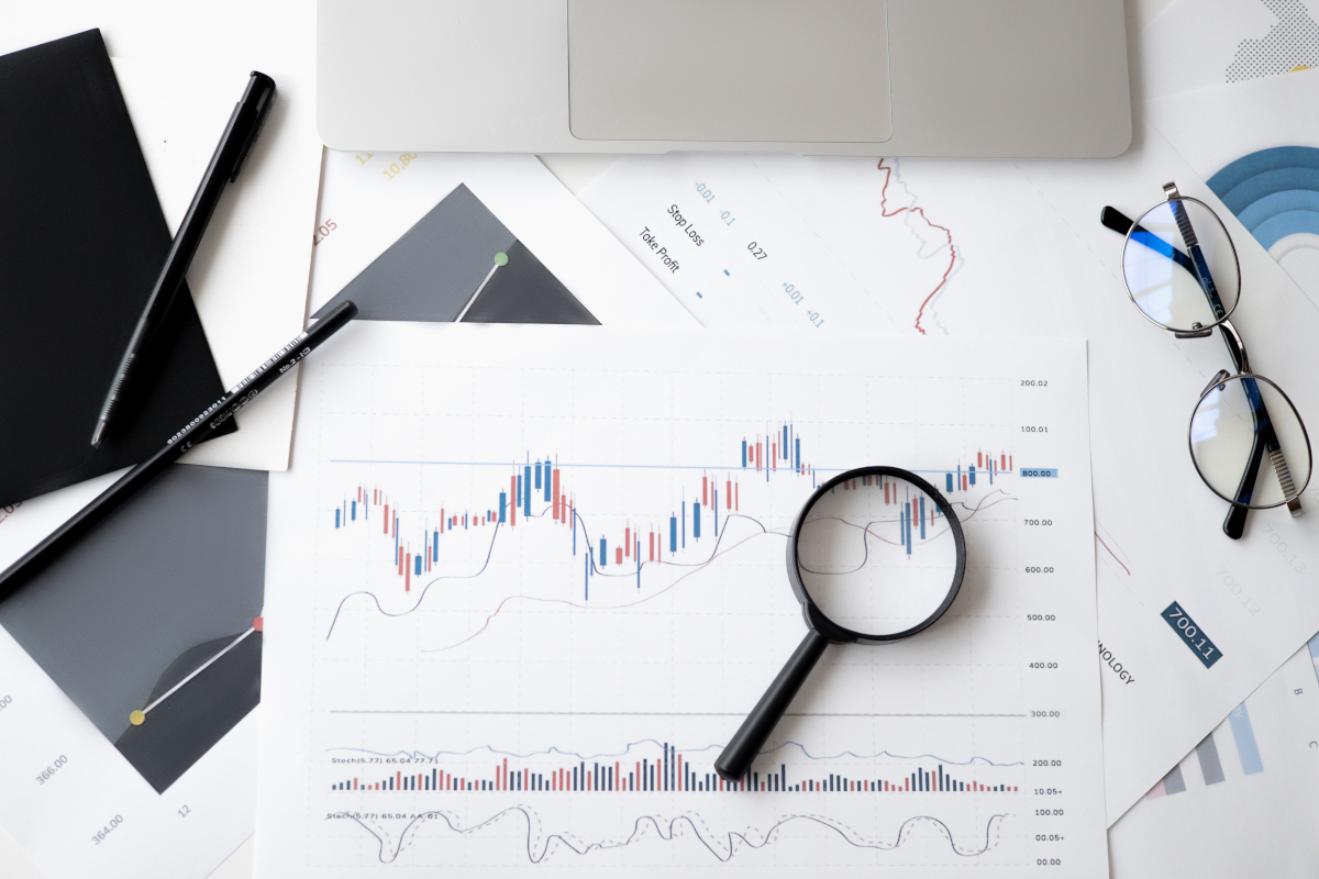 A desk filled with financial documents, charts, and a laptop